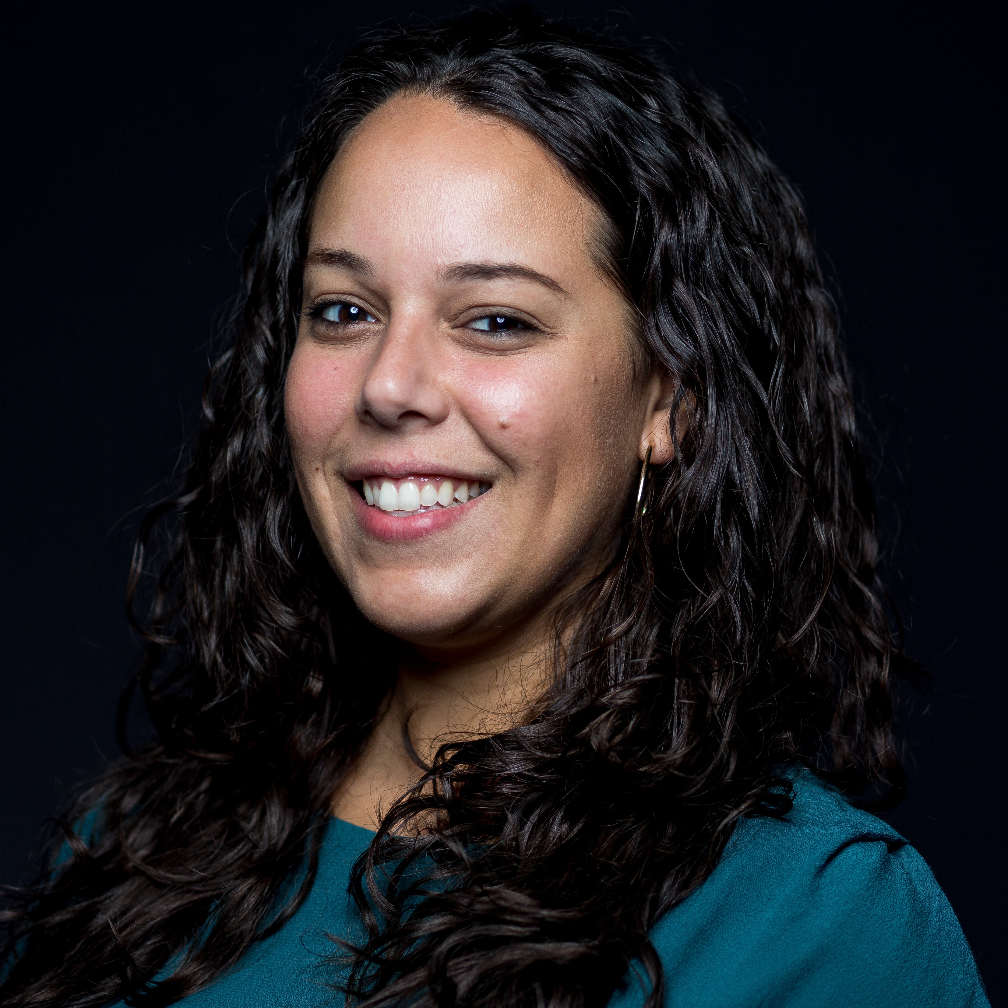A female staff member is posing for a photo with a black backdrop wearing a green shirt, smiling at the camera.